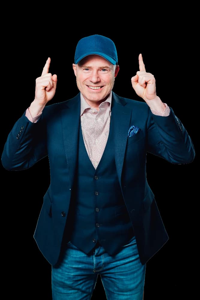 Mike Weiss in a blue cap and navy vest, pointing both index fingers up