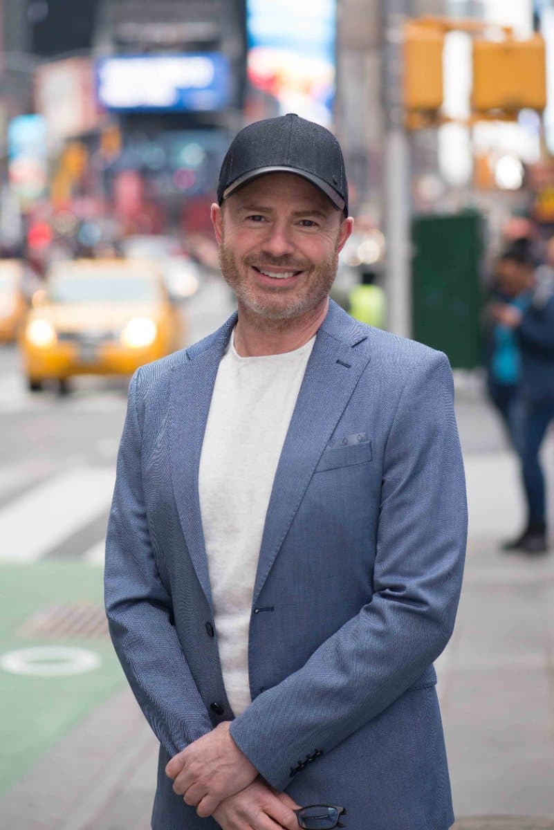 Mike Weiss standing on a Manhattan sidewalk in a dark cap and blue blazer