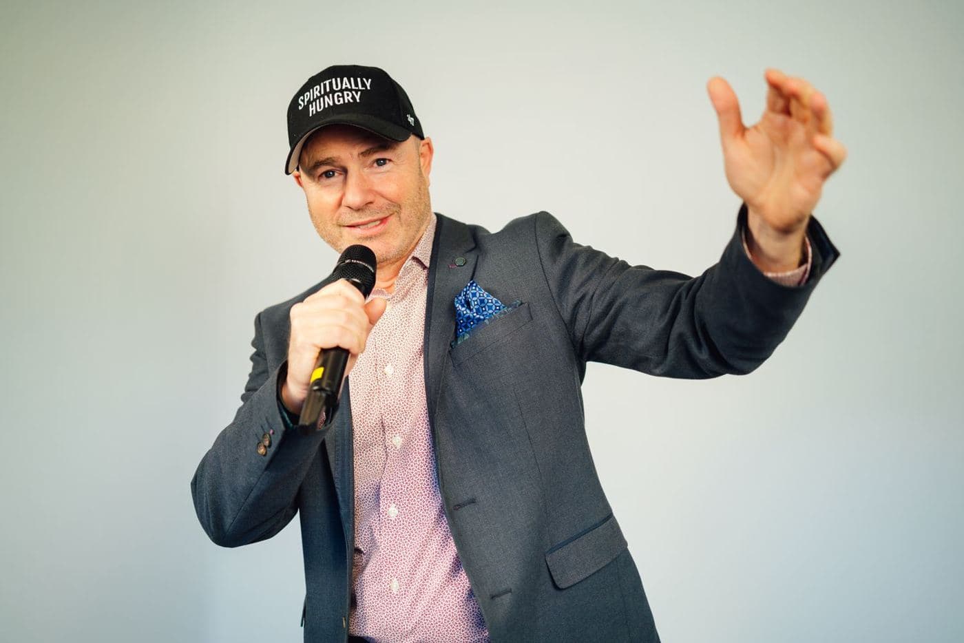 Mike Weiss speaking into a microphone, one hand raised