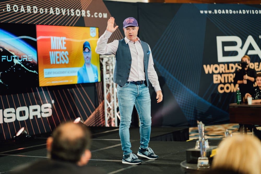 Mike Weiss on stage in a Spread Love cap, waving